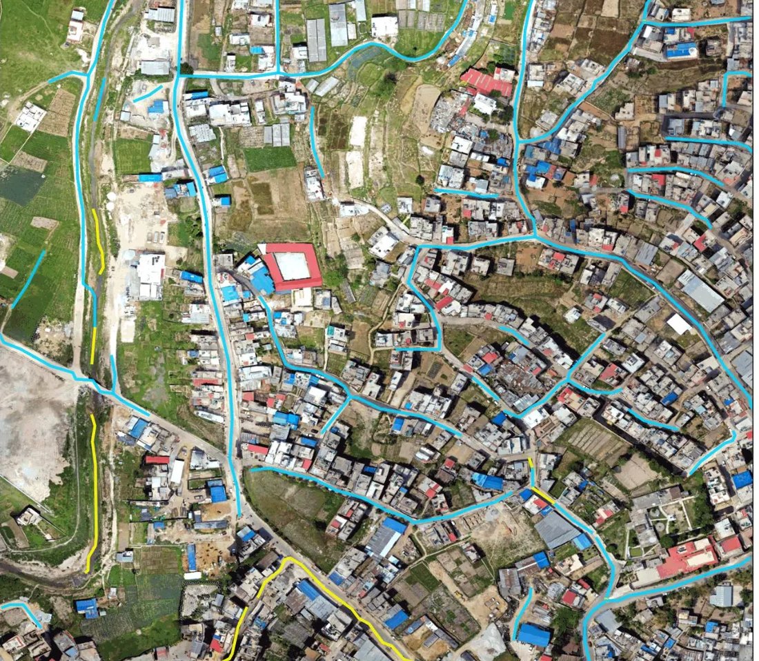Drone view of Banepa, Nepal, a hillside town of dense rooftops and terraced fields, with the model's predicted roads drawn over it as coloured lines